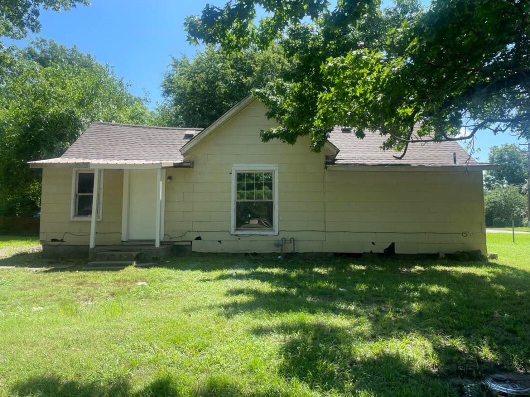 A single-story house with beige siding and a green lawn under a sunny sky.