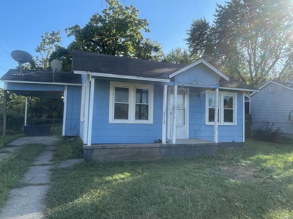 Small blue house with white trim and a carport on a sunny day.