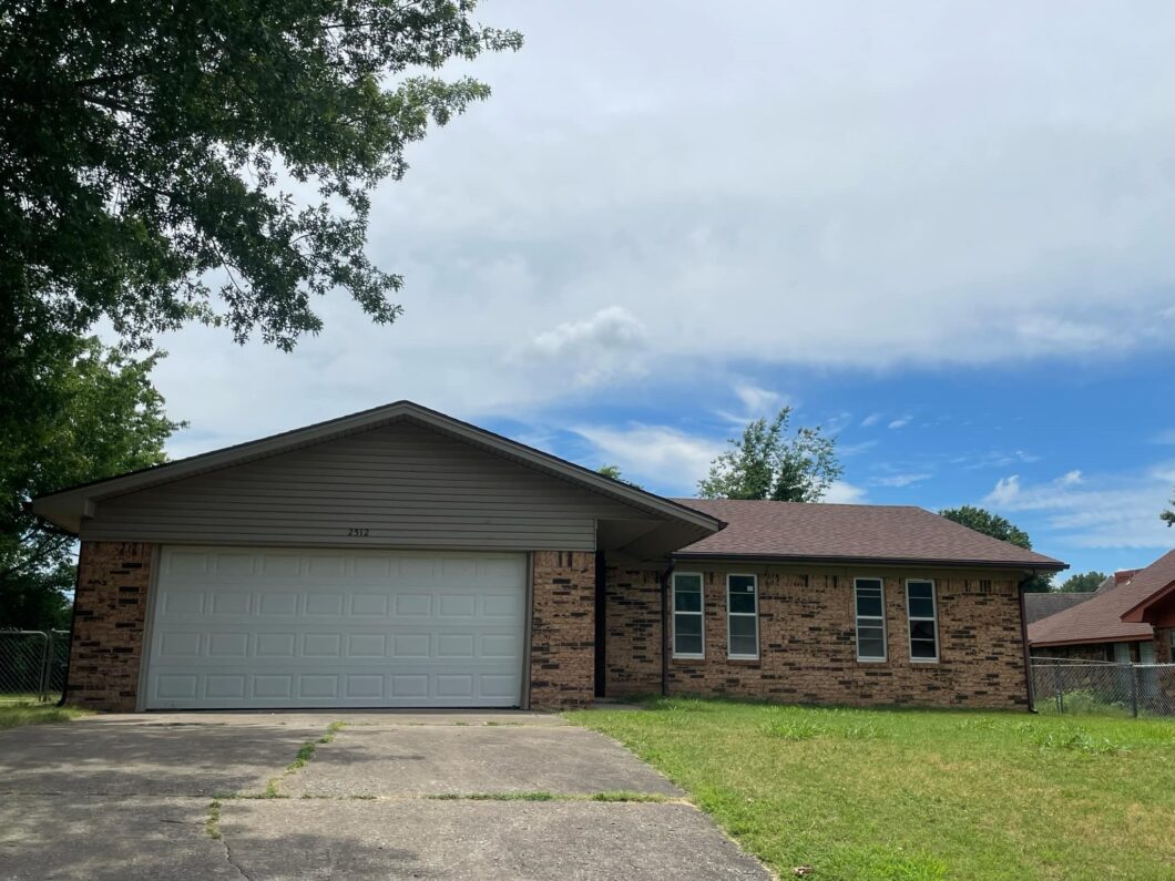 A single-story brick house with a two-car garage and a grassy front yard.
