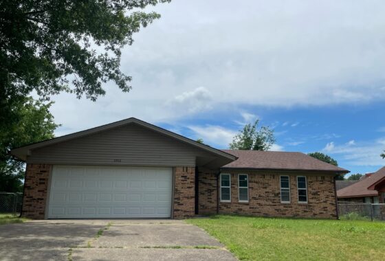 A single-story brick house with a two-car garage and a grassy front yard.